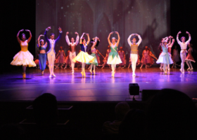 Bailarinos no palco durante apresentação, todos estão com fantasias lembrando de príncipes e princesas da Disney.