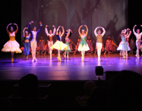 Bailarinos no palco durante apresentação, todos estão com fantasias lembrando de príncipes e princesas da Disney.