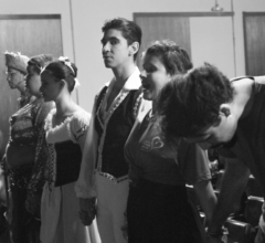 Foto em preto e branco de bailarinos de mãos dadas lado a lado, momentos antes de entrarem no palco para uma apresentação.