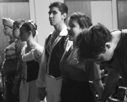 Foto em preto e branco de bailarinos de mãos dadas lado a lado, momentos antes de entrarem no palco para uma apresentação.