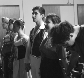 Foto em preto e branco de bailarinos de mãos dadas lado a lado, momentos antes de entrarem no palco para uma apresentação.